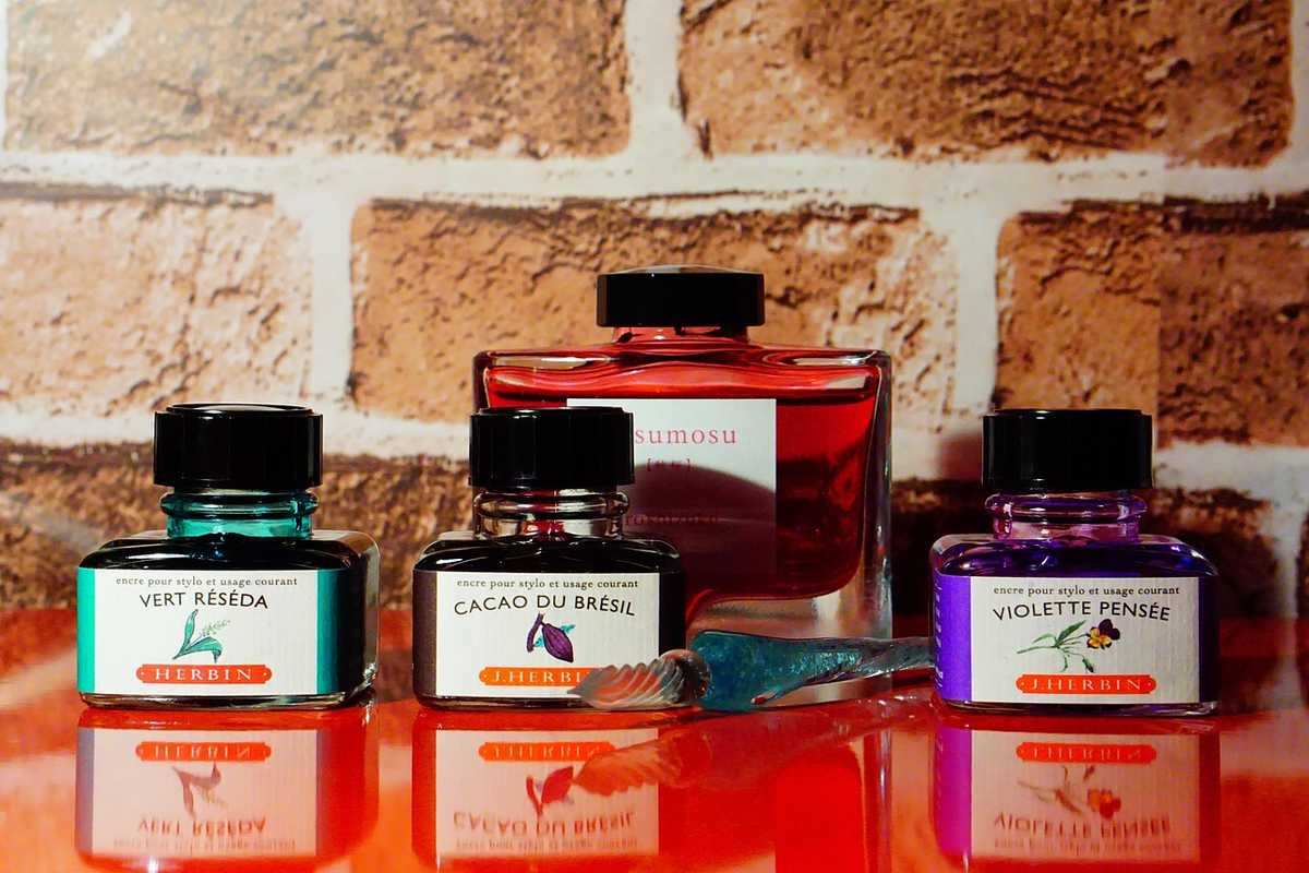 Bouteilles de stylo plume en turquoise, noir, rouge et violet sur une table devant un mur en briques Bouteilles de stylo plume en turquoise, noir, rouge et violet sur une table devant un mur en briques