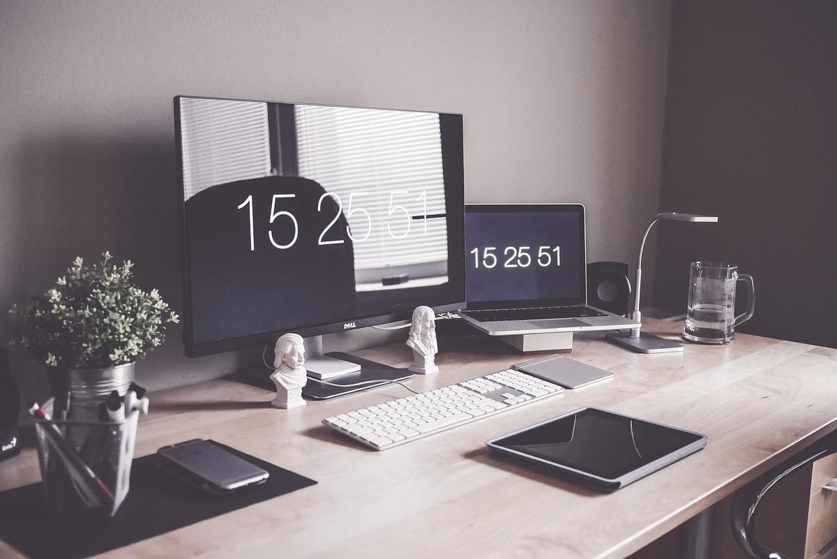 Bureau de travail avec deux écrans affichant l'heure, clavier, plante verte et accessoires